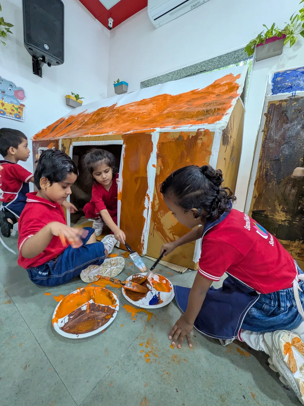 Children painting a play-house with orange paint
