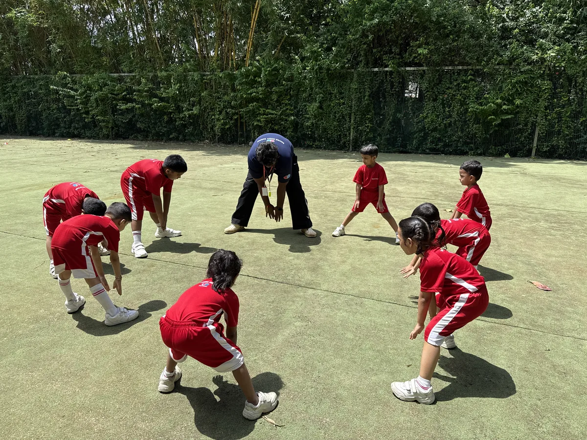 Pre-Primary children stretching in a circle on the field with their coach