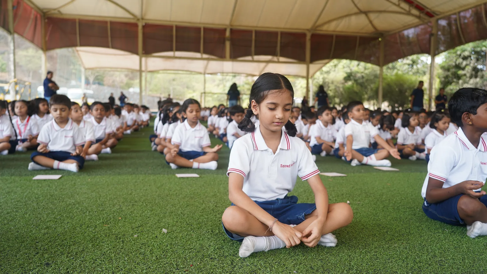 Primary students seated cross-legged outdoors during a Yoga Day session